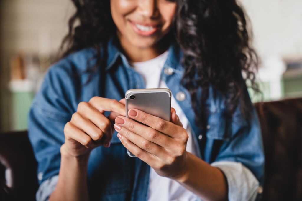 Cropped shot of an african-american young woman using smart phone to compare Bing Ads vs Google Ads.