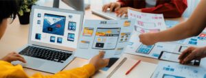 Team reviewing website wireframes and front-end web design layouts on laptops and printed mockups during a website planning session.