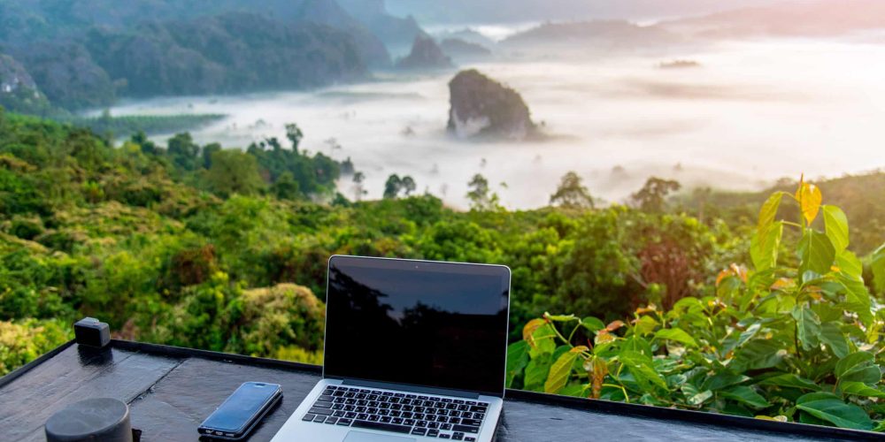 A laptop, mobile  on wooden table with sunrise and mountain fog background in morning. A start of new day. Freelance business concept.